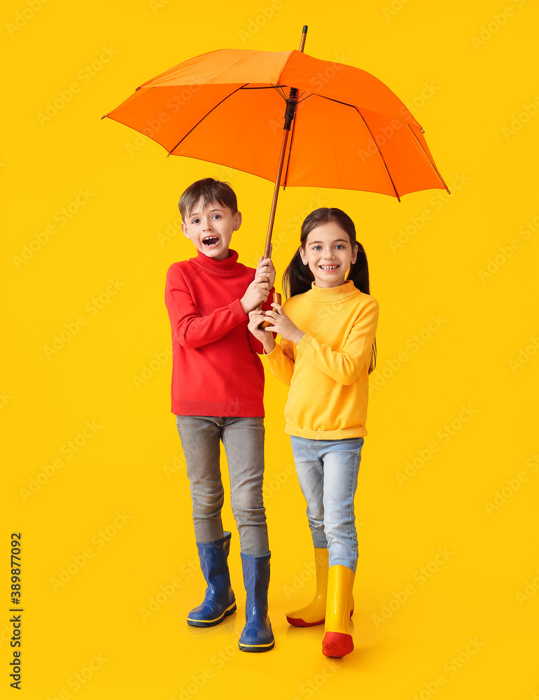 Cute little children in autumn clothes and with umbrella on color background