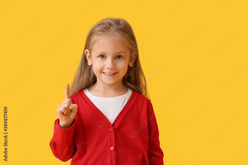 Cute little girl with raised index finger on color background