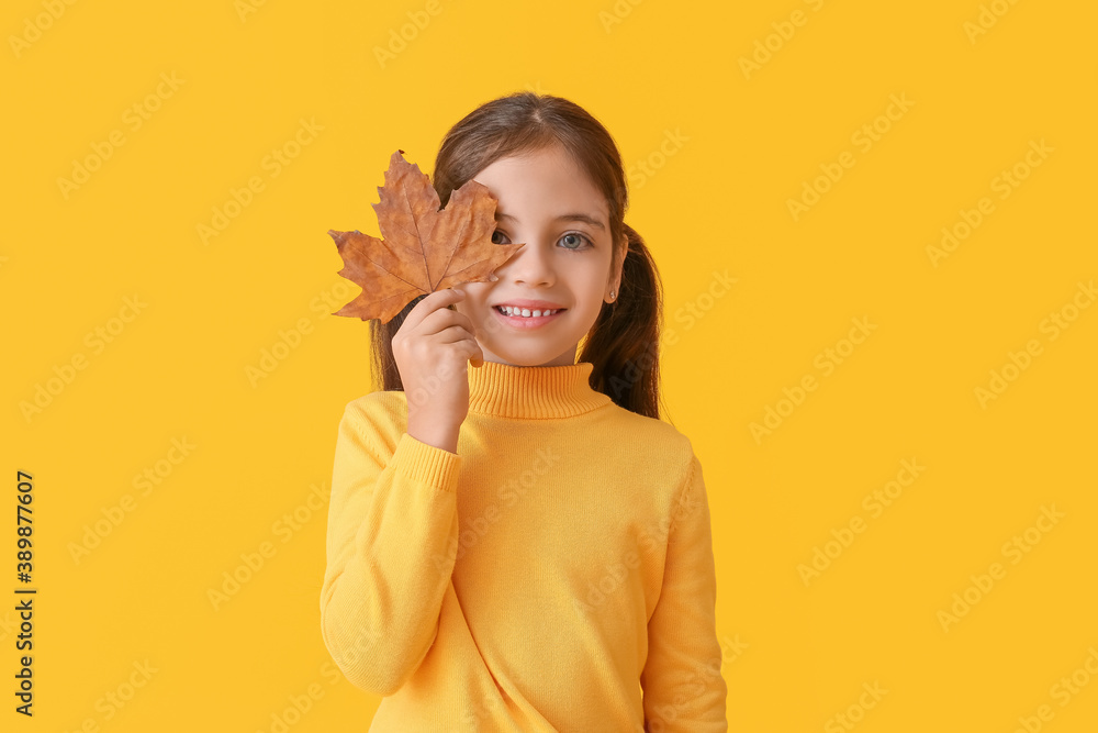 Cute little girl with autumn leaf on color background