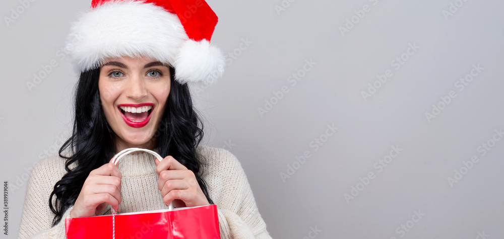 Young woman with santa hat holding a shopping bag on a gray background