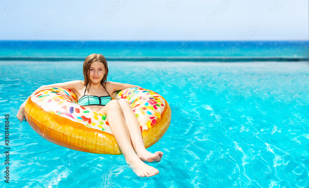 Beautiful girl in sunglasses swim on inflatable doughnut in the pool near the sea