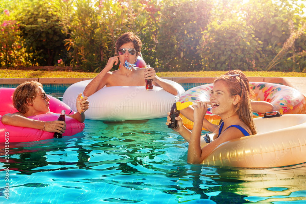 Group of teenage friends kids party drinking soda and blowing noisemakers in swimming pool outside d