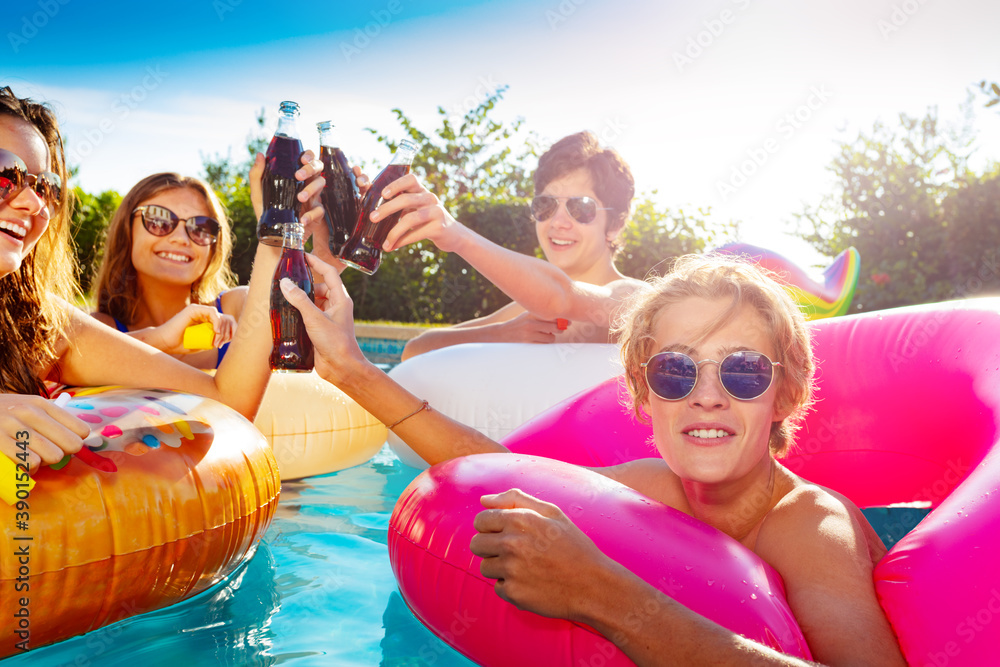 Close photo of teenage children in water party with soda drink, lift hands and swim in inflatable do