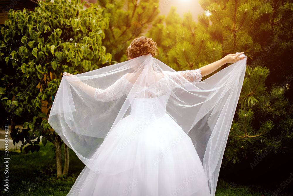 The bride holds a wedding veil on a green natural background