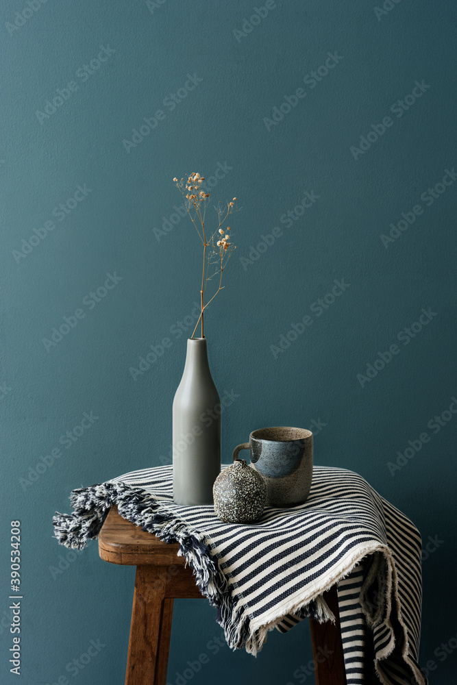 Gray ceramic vase with a mug on a wooden stool by a forest green wall