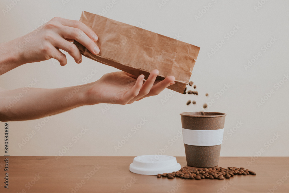 Hand pouring coffee beans from a paper bag into a coffee cup