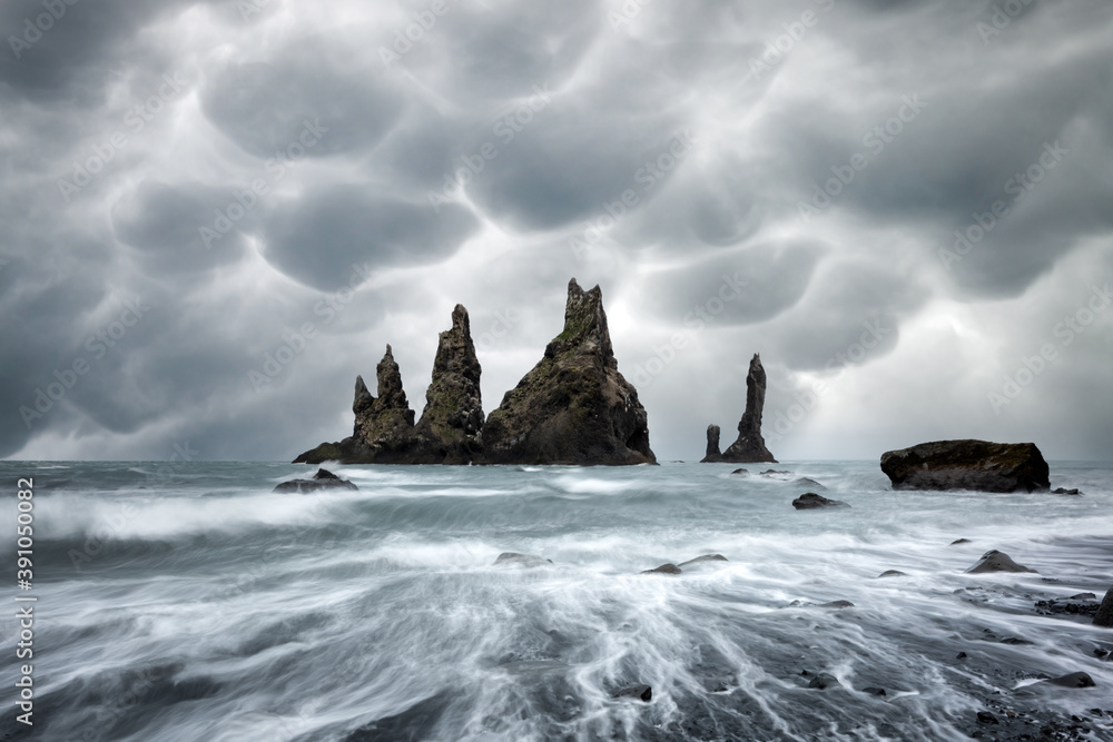 玄武岩岩层Troll toes on black beach with暴风雨般的天空，ba上有威胁性的长毛象云