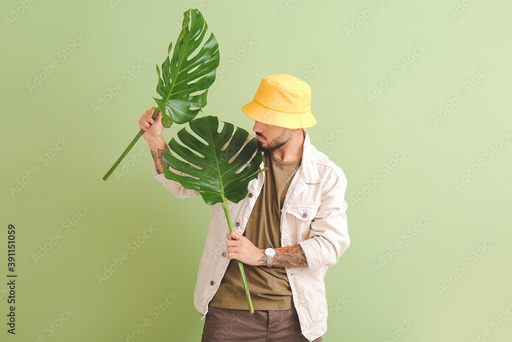 Fashionable young man with tropical leaves on color background