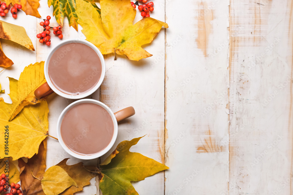 Cup of hot cacao drink with autumn leaves on white wooden background