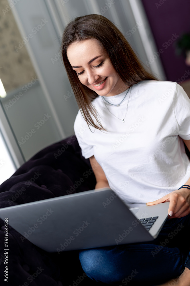 Woman in living room sitting on sofa using laptop. Smiling young beautiful girl.