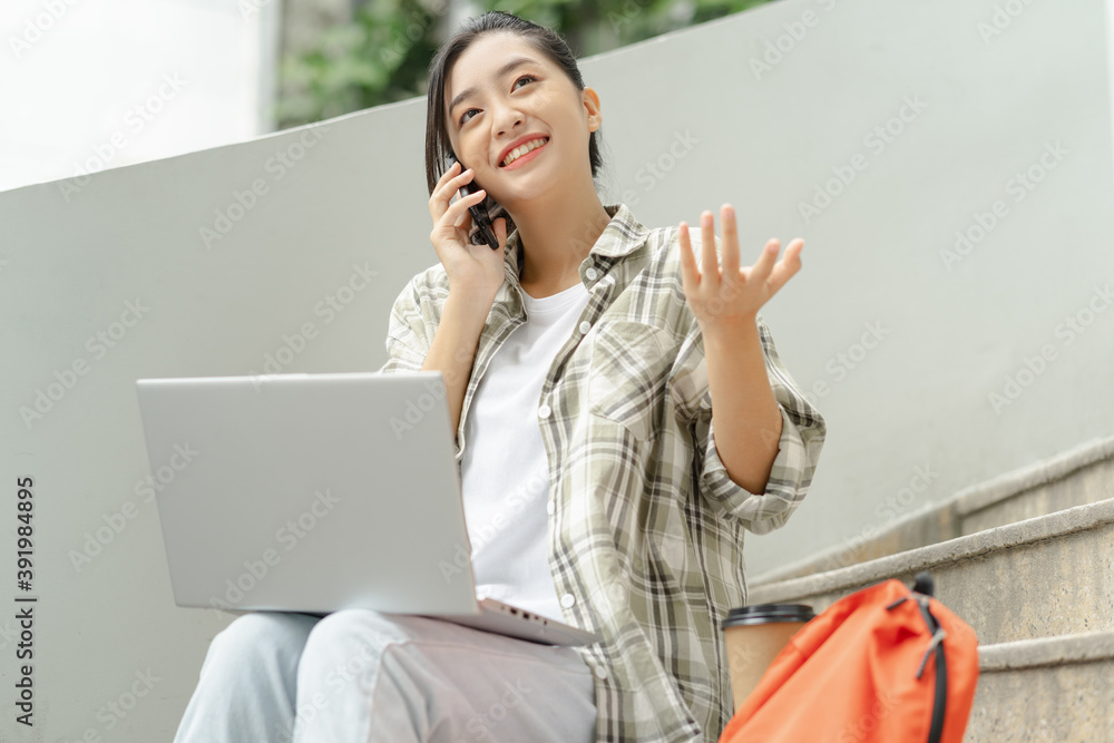 女学生正在学校的楼梯上学习和听电话