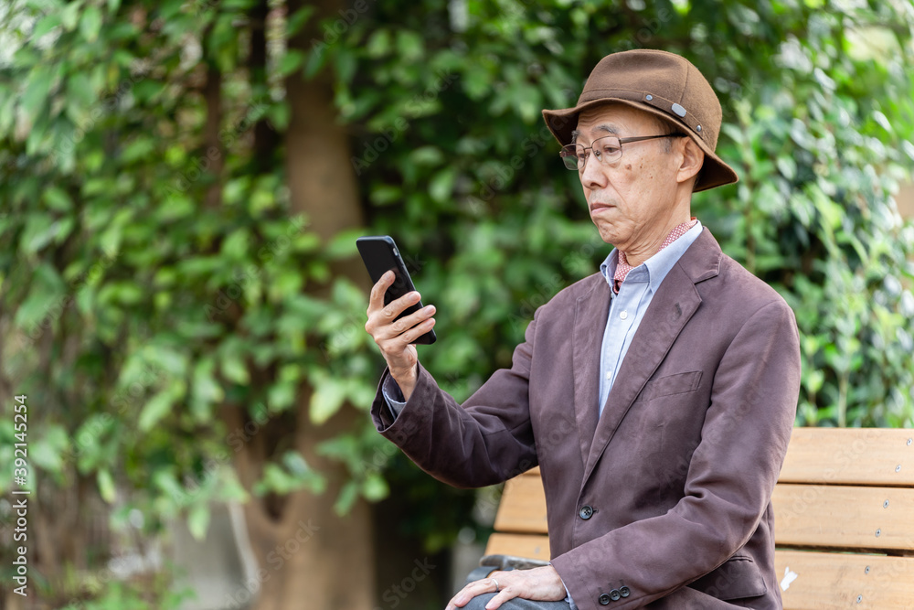 公園でスマートフォンを使うシニア男性