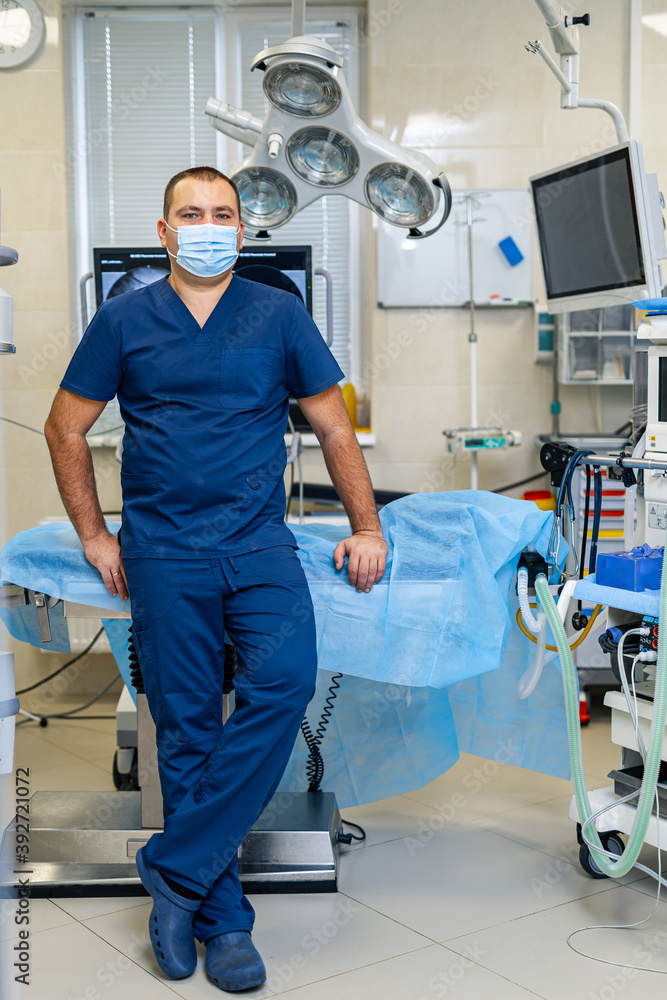 Young confident male doctor poses to the camera on modern surgery room background. Health care and l