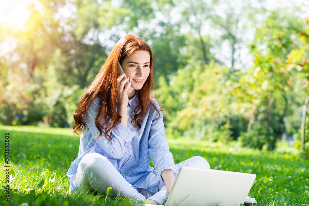 Young redhead woman sitting on green grass