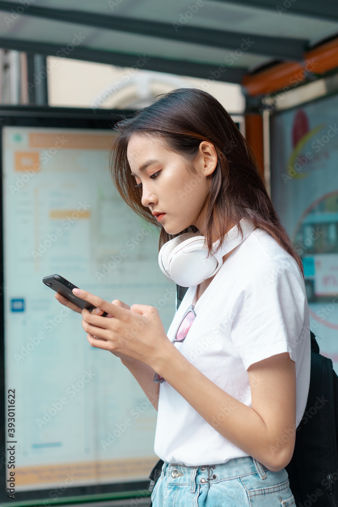 漂亮的亚洲女孩在等公交车时用手机