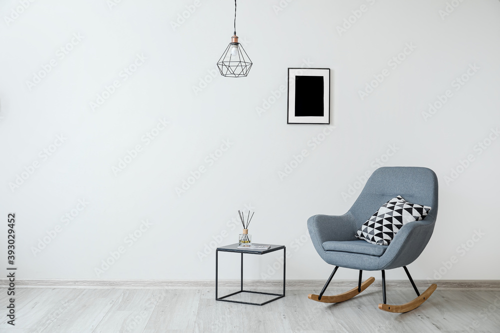 Stylish armchair with pillow and table near light wall in room