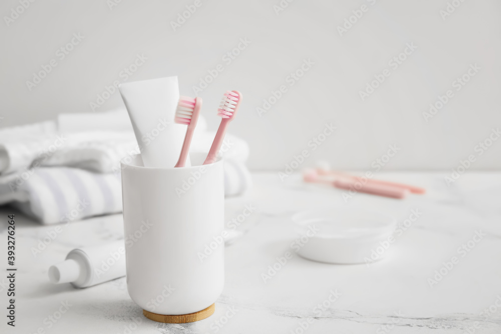 Holder with toothbrushes and paste on table in bathroom