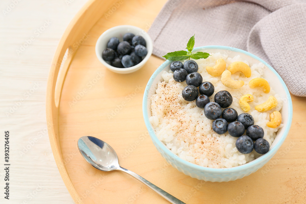 Bowl of tasty rice pudding with blueberry and cashew on wooden tray