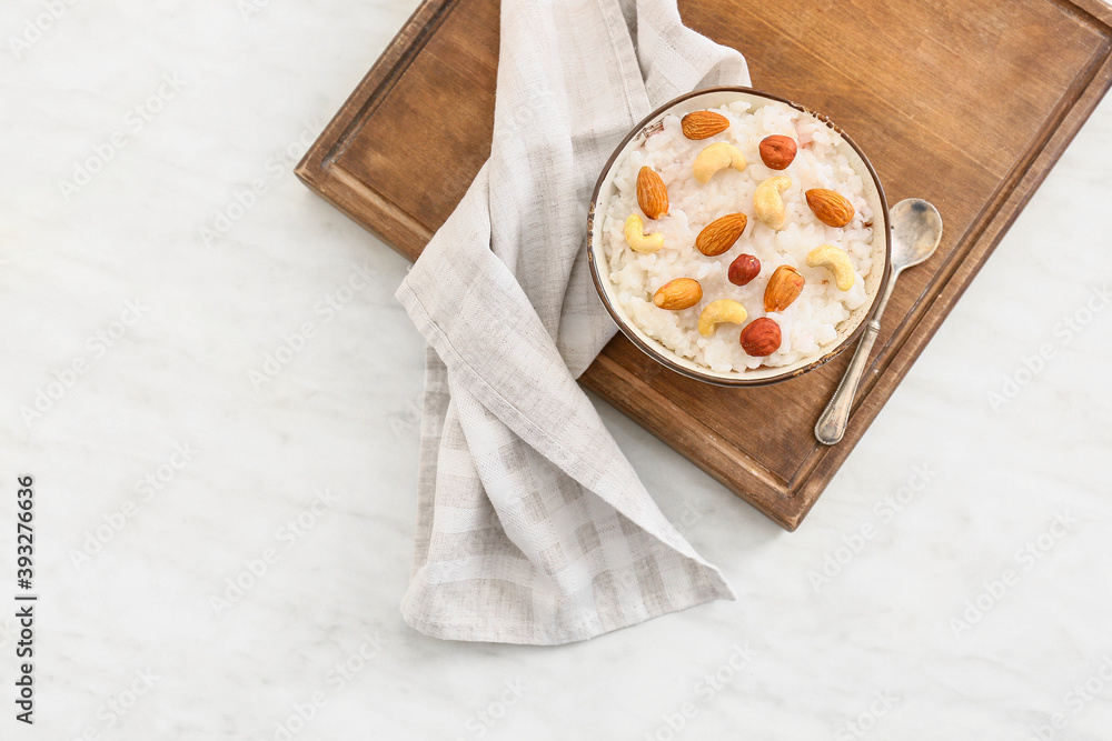 Bowl of tasty rice pudding with nuts on wooden board