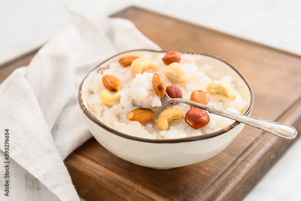 Bowl of tasty rice pudding with nuts on wooden board