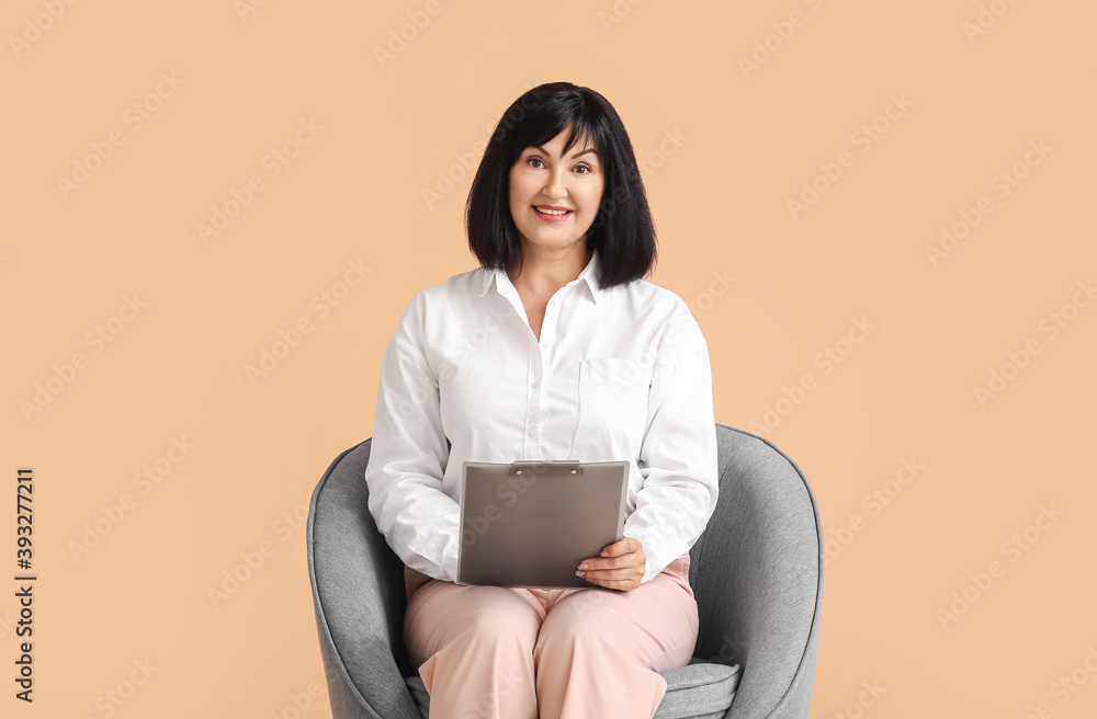 Portrait of female psychologist sitting in armchair on color background