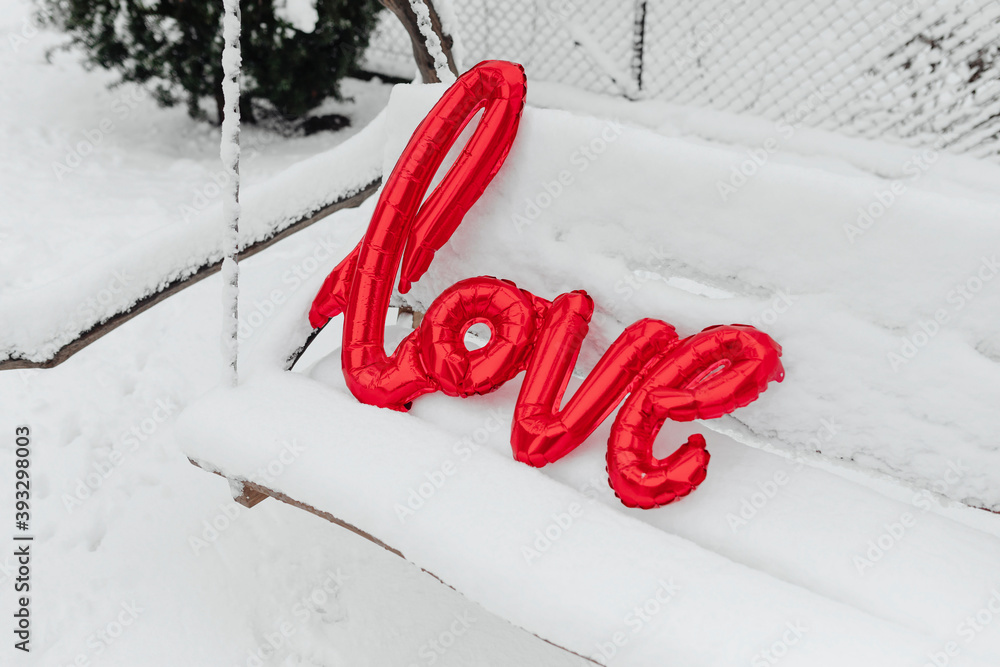 Red love balloon word on a snowy swing