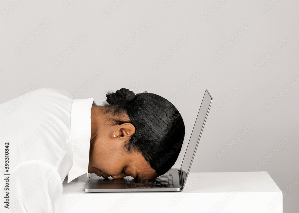 Tired black woman resting her head on a laptop