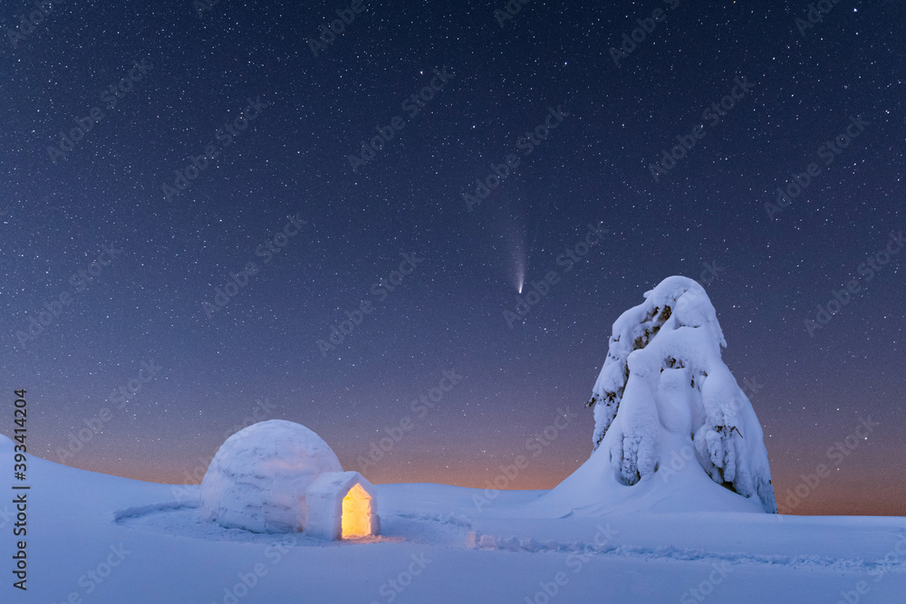 冬季山脉中从内部发光的雪冰屋。背景是彗星的星空