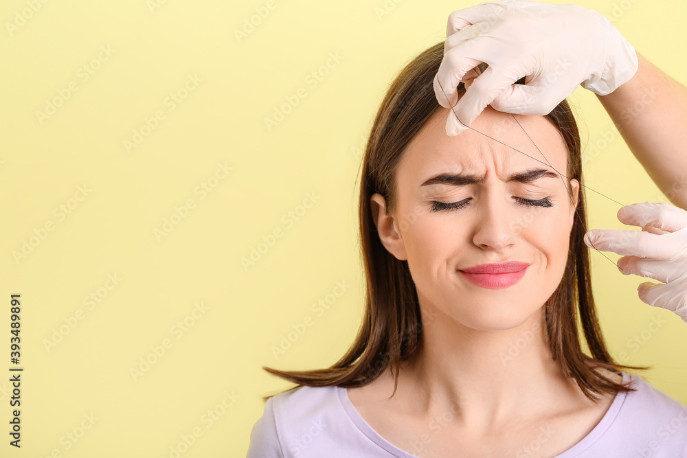 Young woman undergoing eyebrow correction procedure on color background