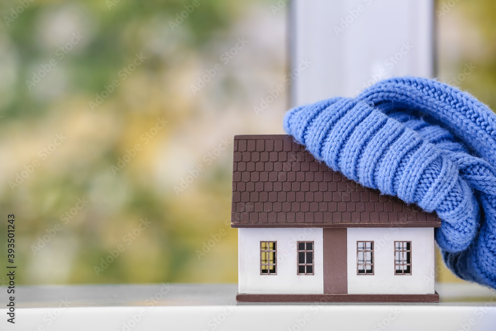 Figure of house and warm hat on window sill. Concept of heating season