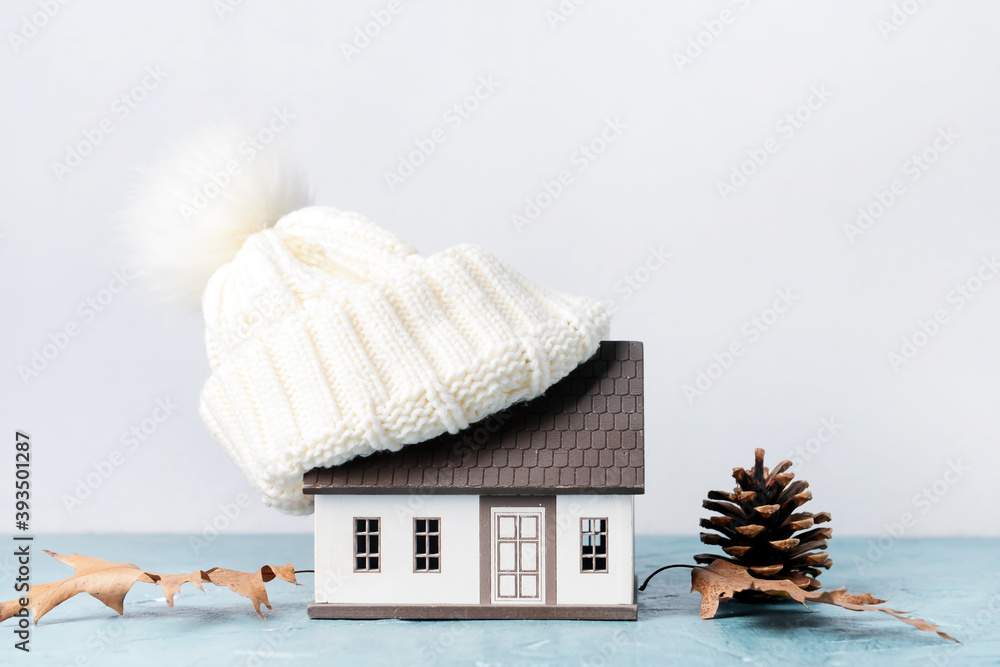 Figure of house, autumn leaves and warm hat on table. Concept of heating season