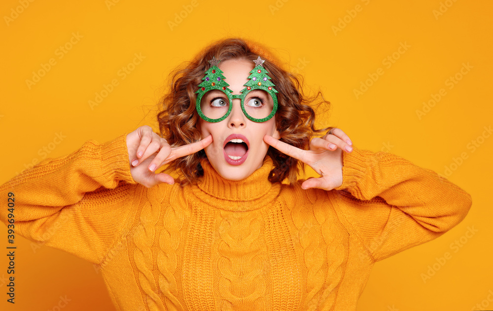 funny cheerful   woman in silly glasses with Christmas trees on a   yellow background