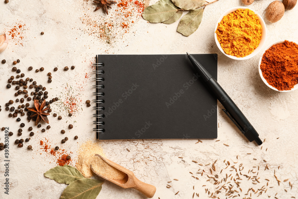 Black notebook and set of spices on white table