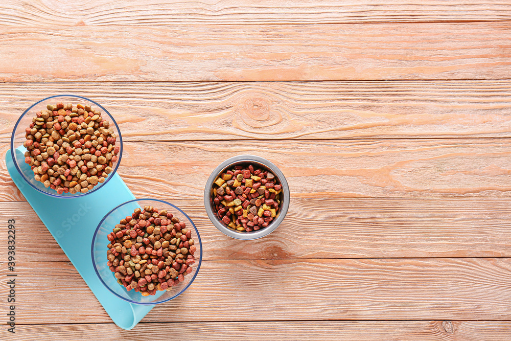 Bowls with dry pet food on wooden background