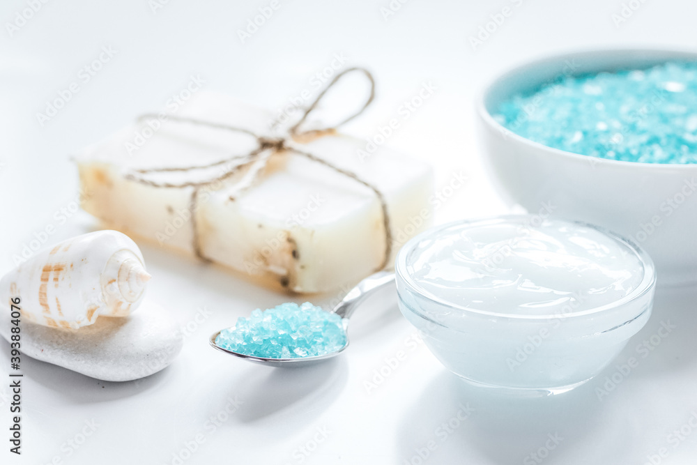 blue bath salt, body cream and shells for spa on white table background