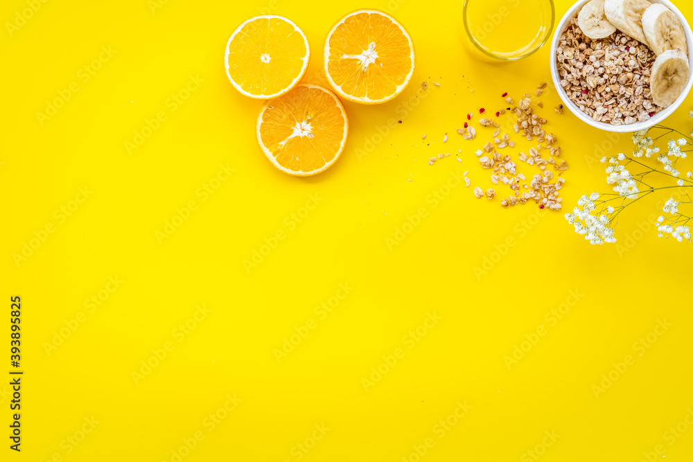 Healthy granola with banana and orange juice for colorful breakfast on yellow background top view mo