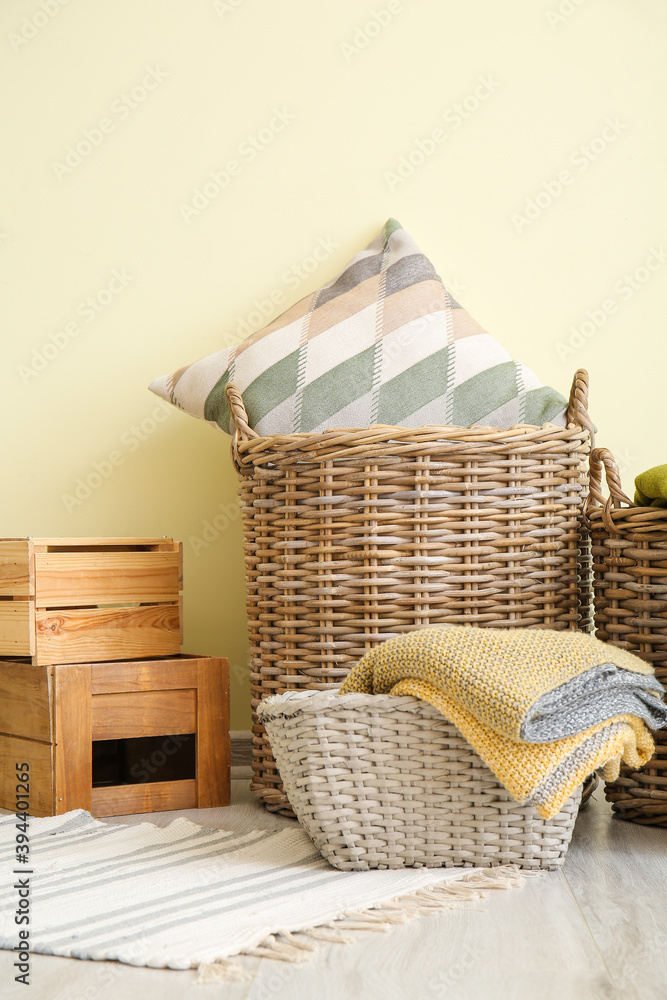 Wicker baskets with pillow, plaid and boxes on floor near color wall