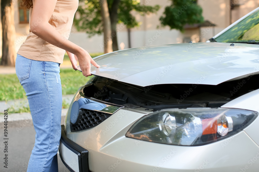 Young woman opening hood of her car outdoors