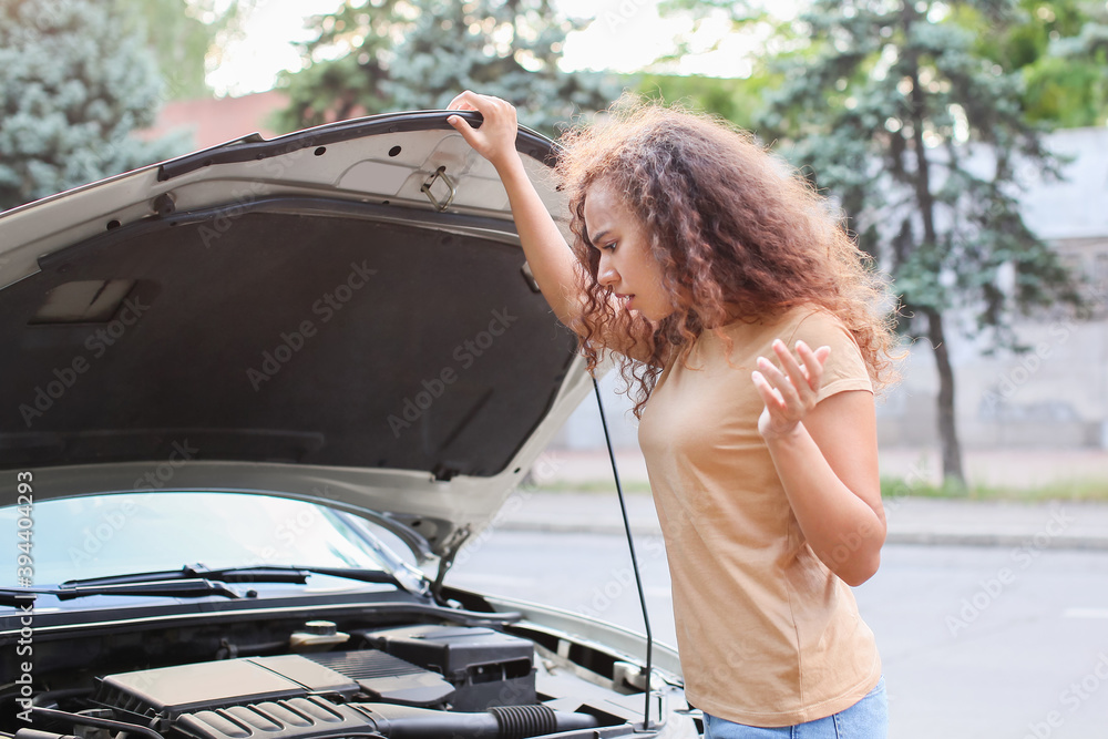 Stressed African-American woman near broken car outdoors