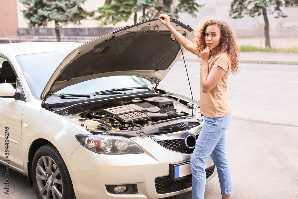 Stressed African-American woman near broken car outdoors