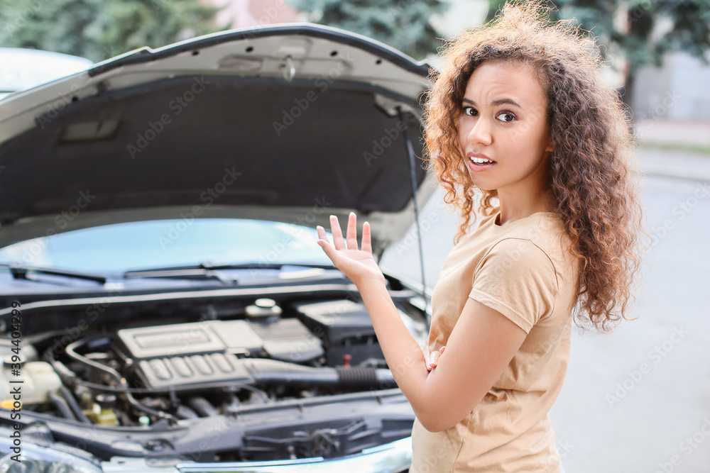 Stressed African-American woman near broken car outdoors