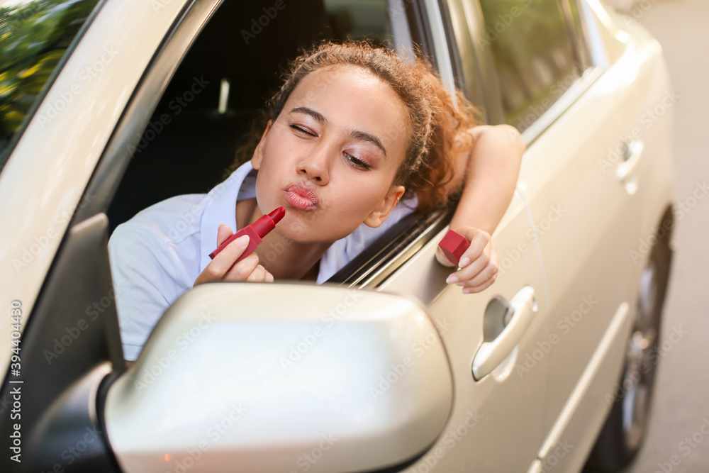 Beautiful African-American woman applying lipstick while sitting in car