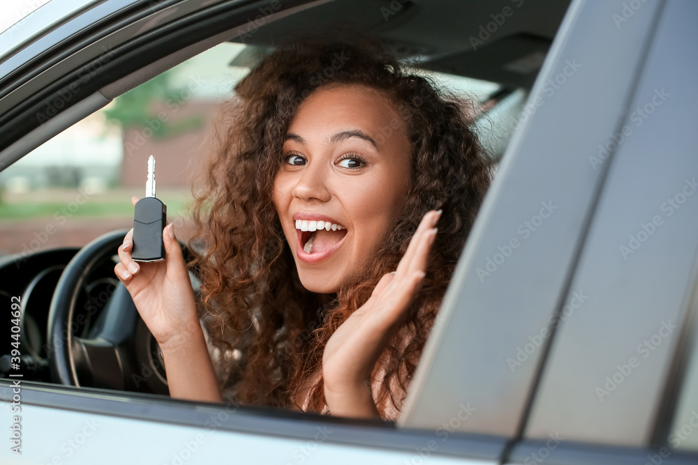 Happy African-American woman with key sitting in new car