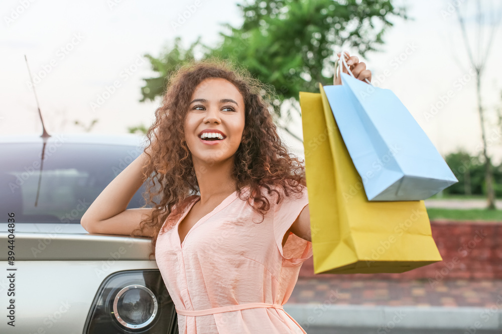 Young African-American woman with shopping bags near car outdoors