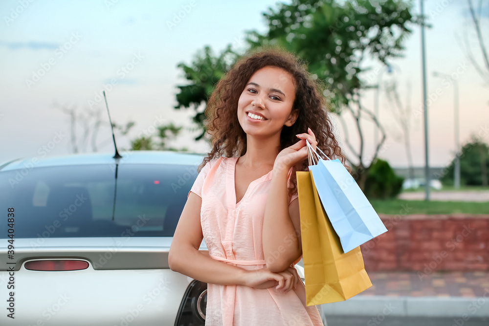 Young African-American woman with shopping bags near car outdoors