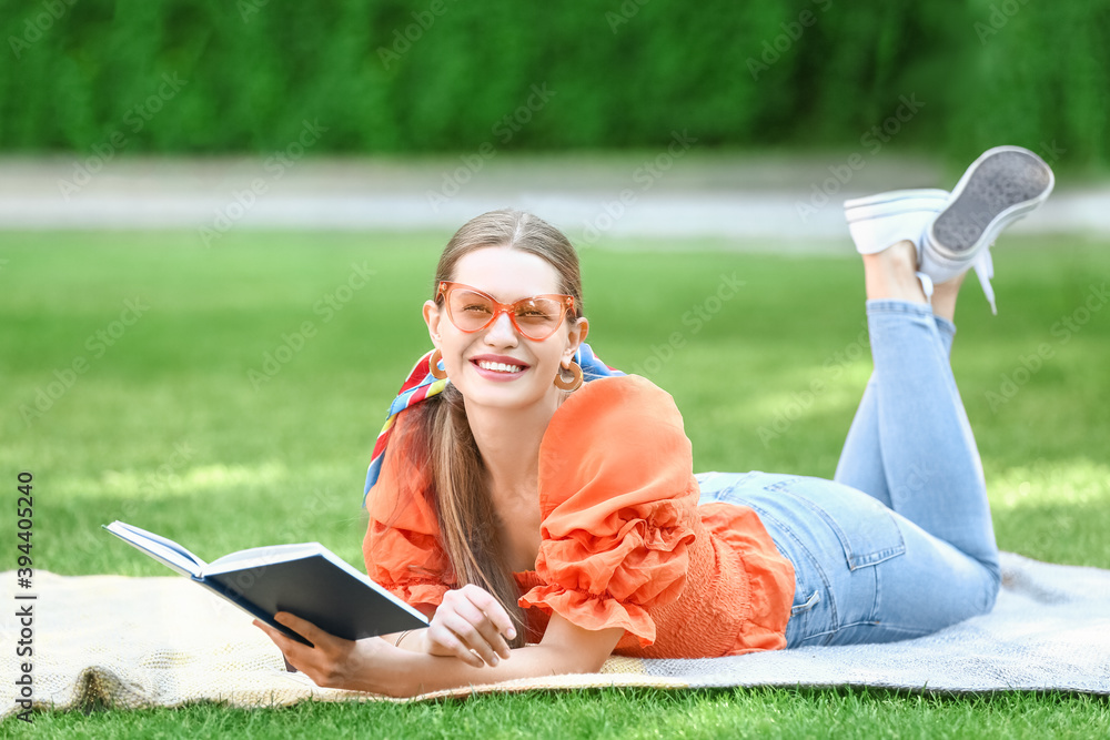 Beautiful young woman reading book while relaxing in park