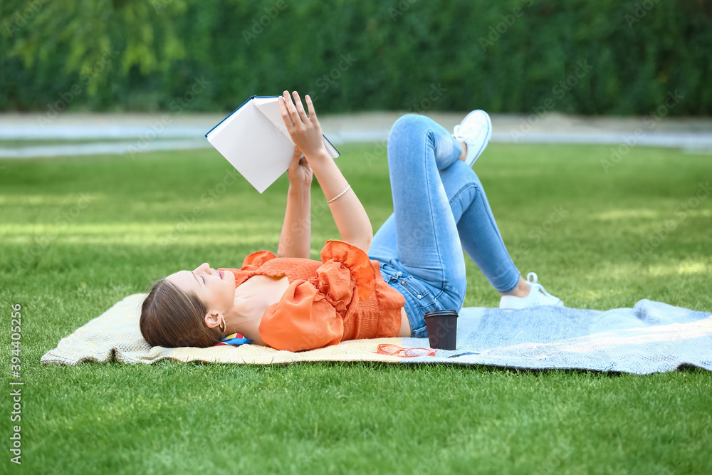 Beautiful young woman reading book while relaxing in park