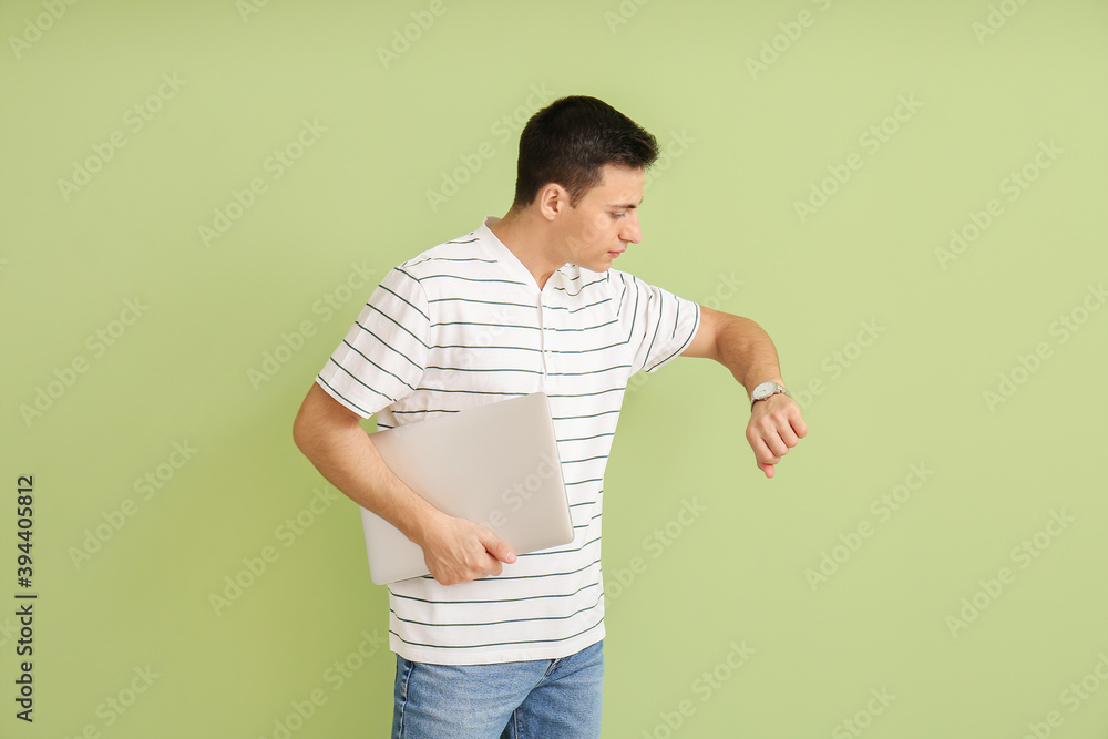 Young man with wristwatch and laptop on color background