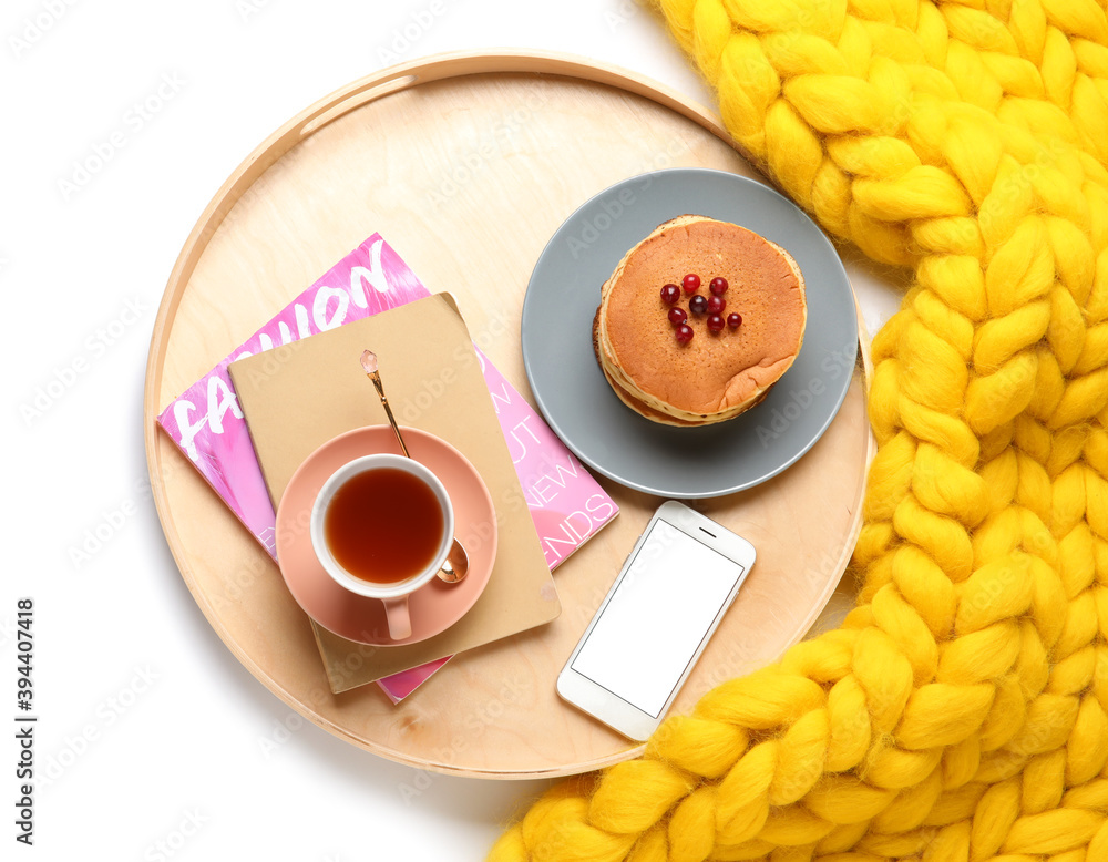 Tray with tasty breakfast, mobile phone and knitted plaid on white background