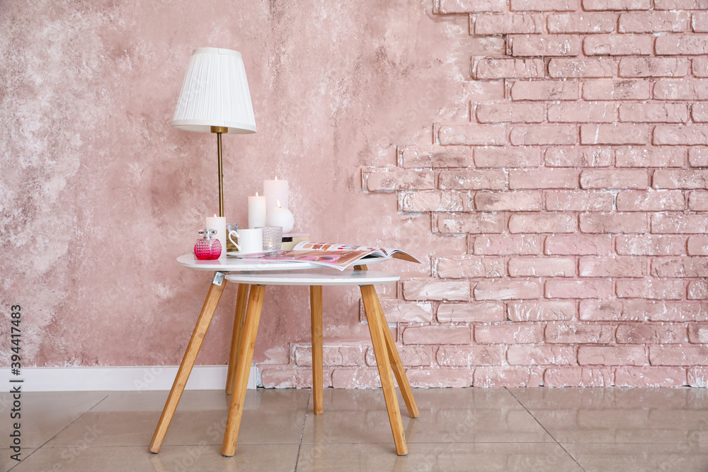 Burning candles, fashion magazine and lamp on table in room